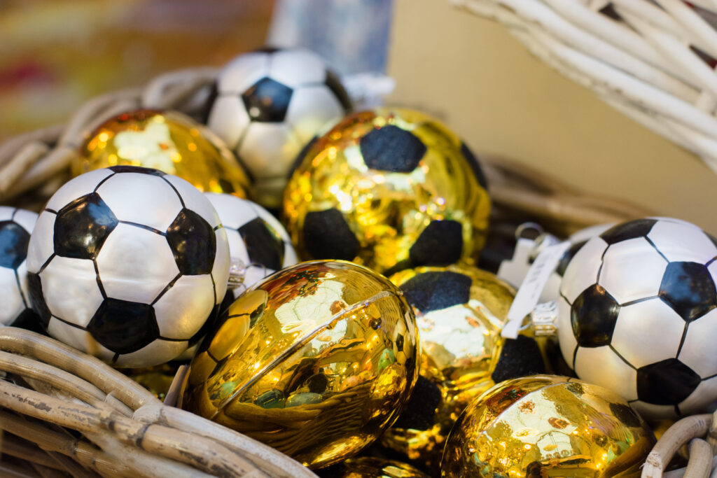 Cesta com bolas de futebol decorativas em preto, branco e dourado, representando decoração temática para a Copa do Mundo.
