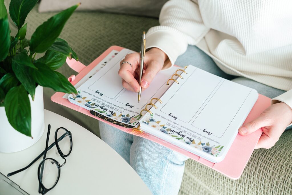 Mulher escrevendo em planner personalizado rosa, tendência de papelaria personalizada.