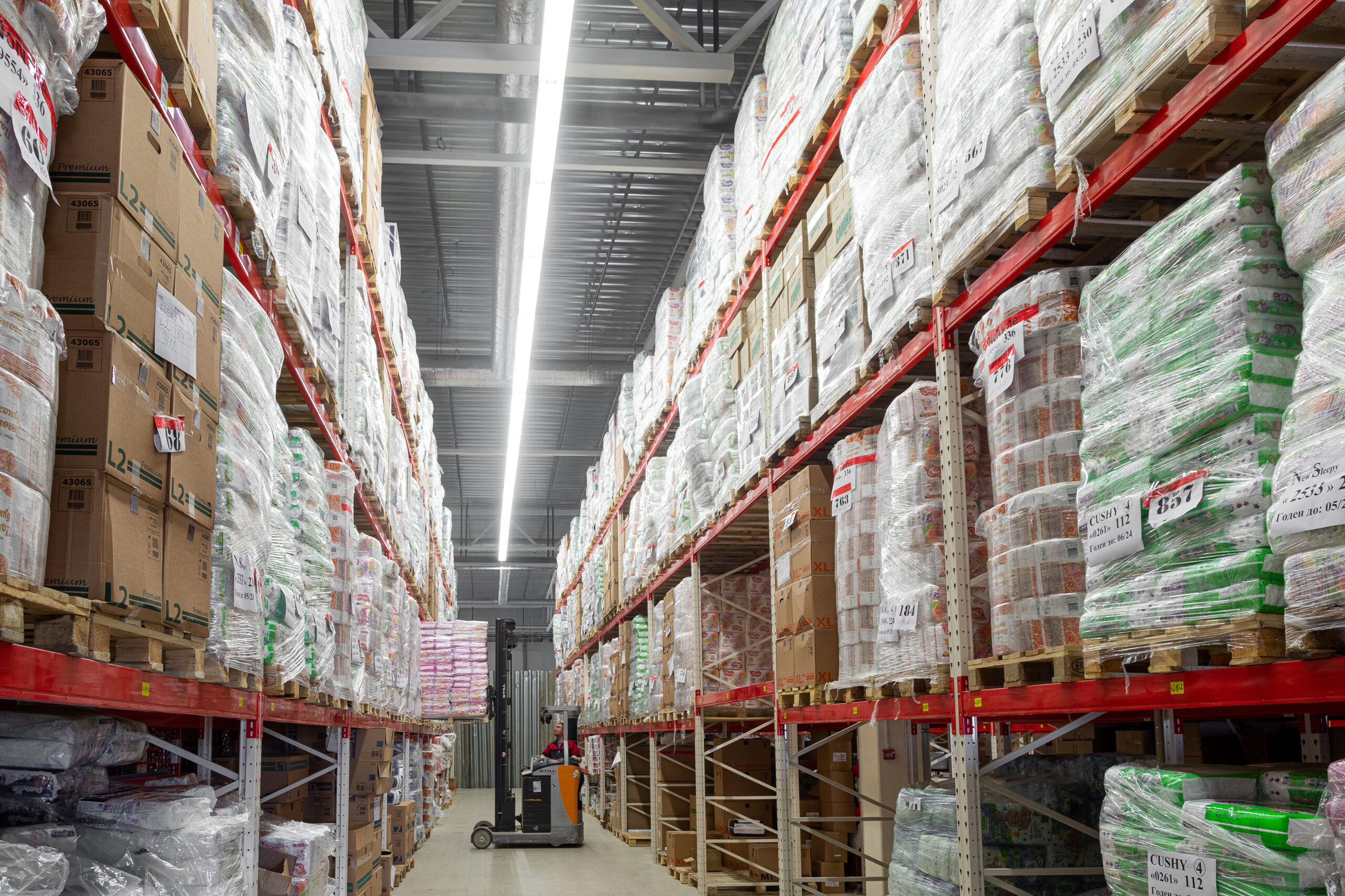 Depósito com grandes volumes de produtos empilhados em pallets, representando o conceito de atacado no varejo brasileiro.