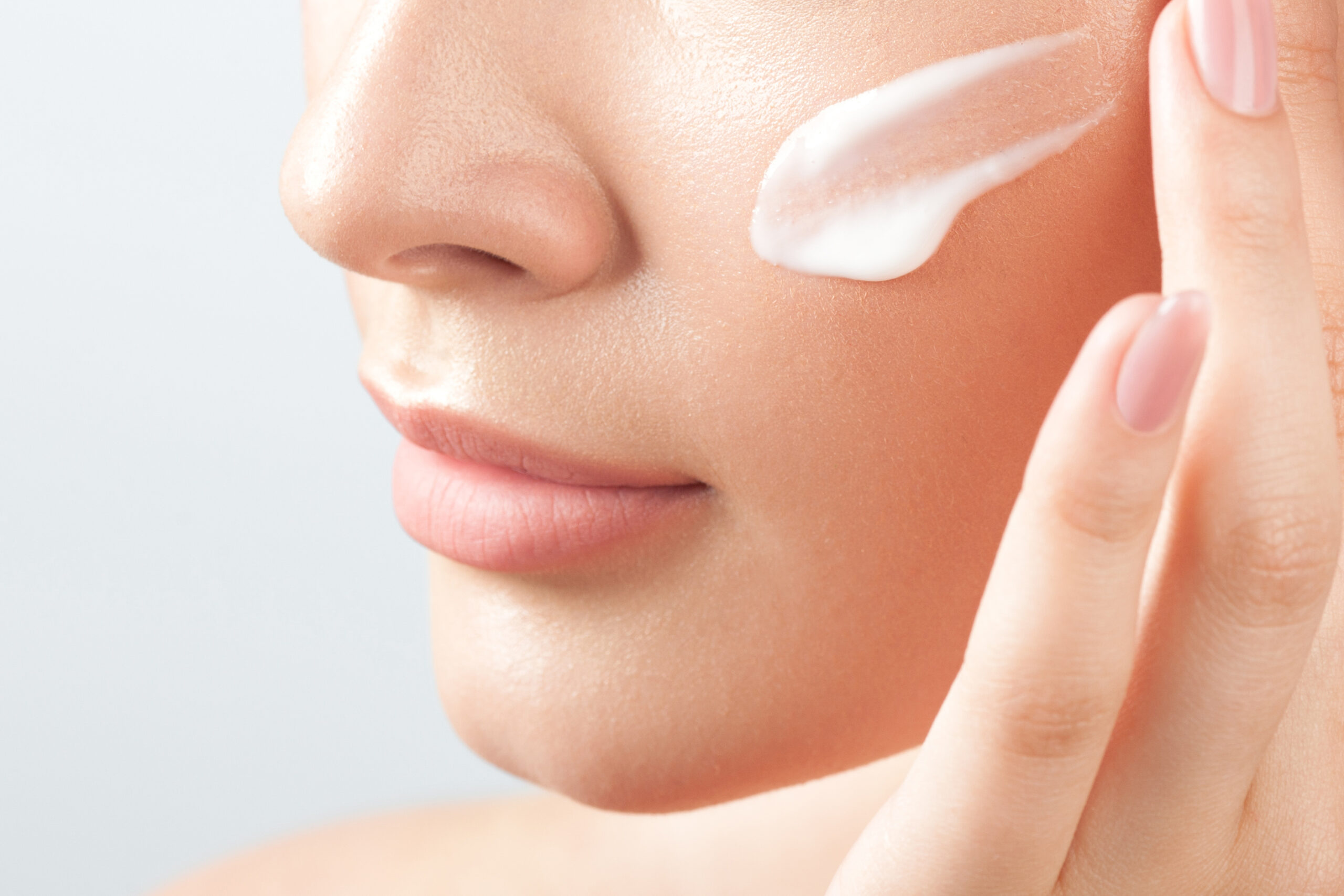 Mulher sorridente aplicando creme hidratante no rosto, ilustrando a rotina de cuidados com a pele no inverno. Post sobre  Cuidados com a pele no inverno: Monte o mix perfeito e lucre no seu comércio!