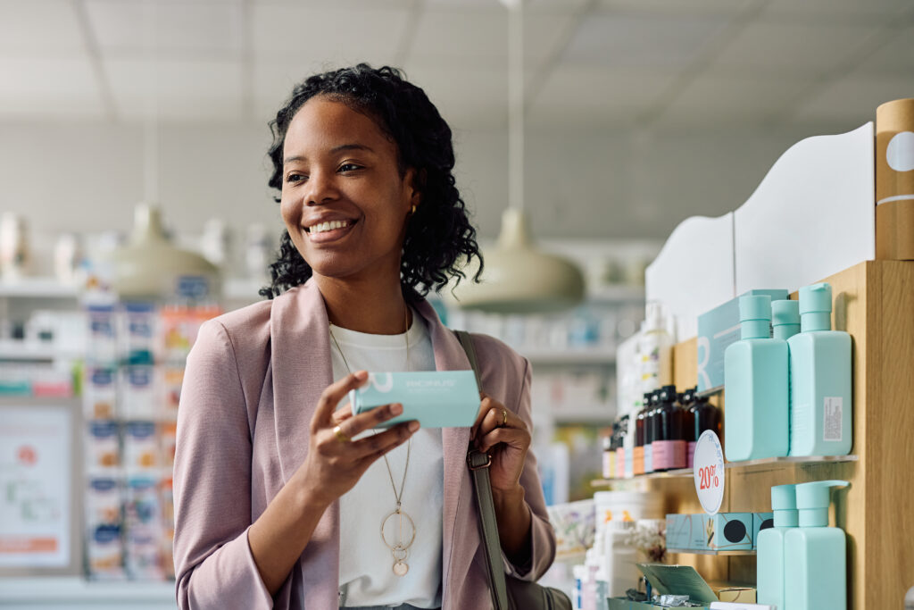 Mulher segurando produto de skincare em frente à prateleira de exposição em uma loja de cosméticos. Ilustrando o post sobre  Cuidados com a pele no inverno: Monte o mix perfeito e lucre no seu comércio!