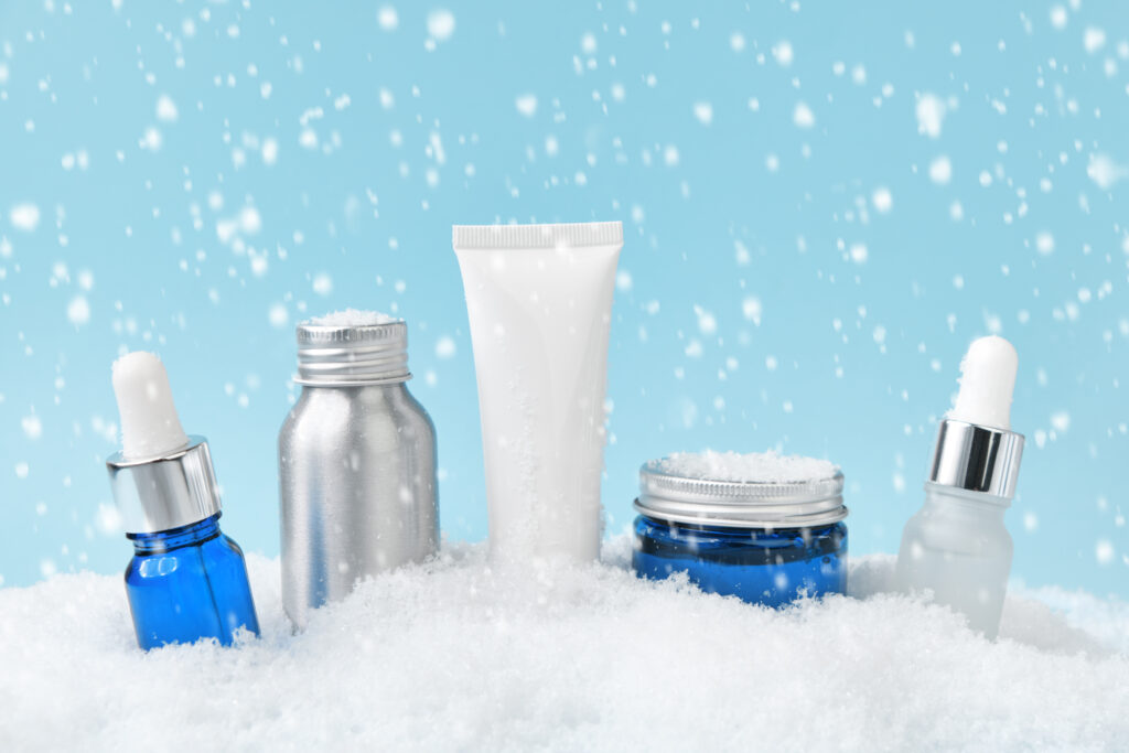  Embalagens de cosméticos e produtos de skincare para o inverno dispostos sobre neve artificial. Ilustrando o post sobre  Cuidados com a pele no inverno: Monte o mix perfeito e lucre no seu comércio!